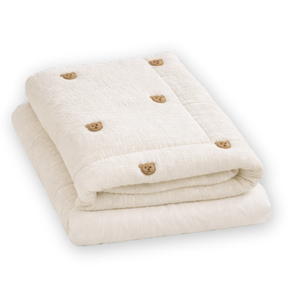 Cream-colored baby blanket neatly folded with small brown bear face embroidery pattern.