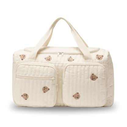 Cream-colored diaper bag with stitched bear faces and two front zippered pockets.