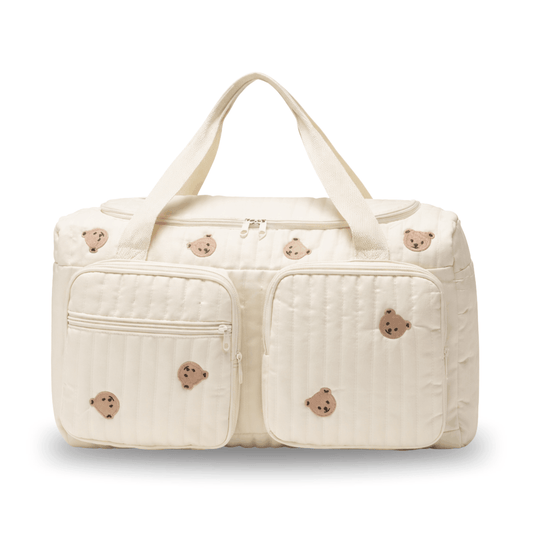 Cream-colored diaper bag with stitched bear faces and two front zippered pockets.