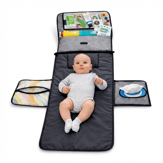 Baby lying on a black portable changing pad with side pockets and organized baby care items.